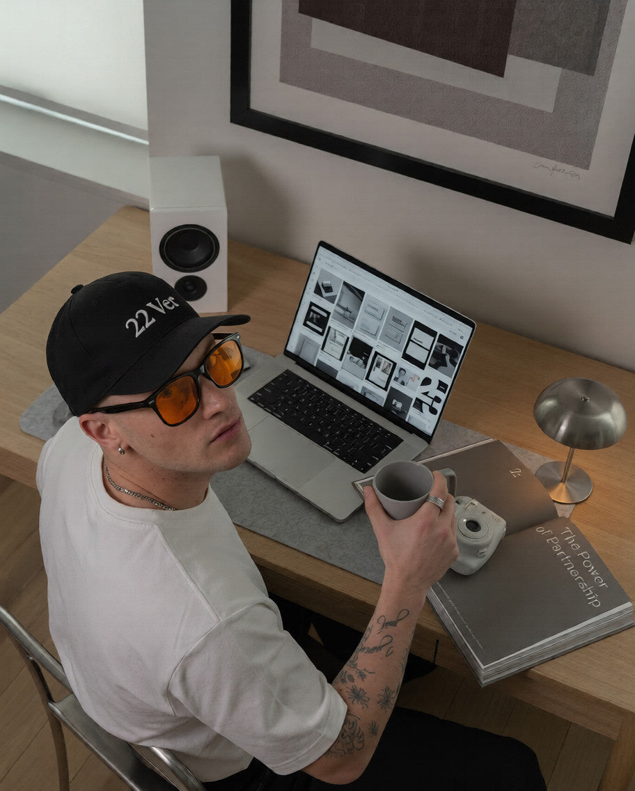 Man in a orange day blue light blocking glasses and a black cap working on a laptop